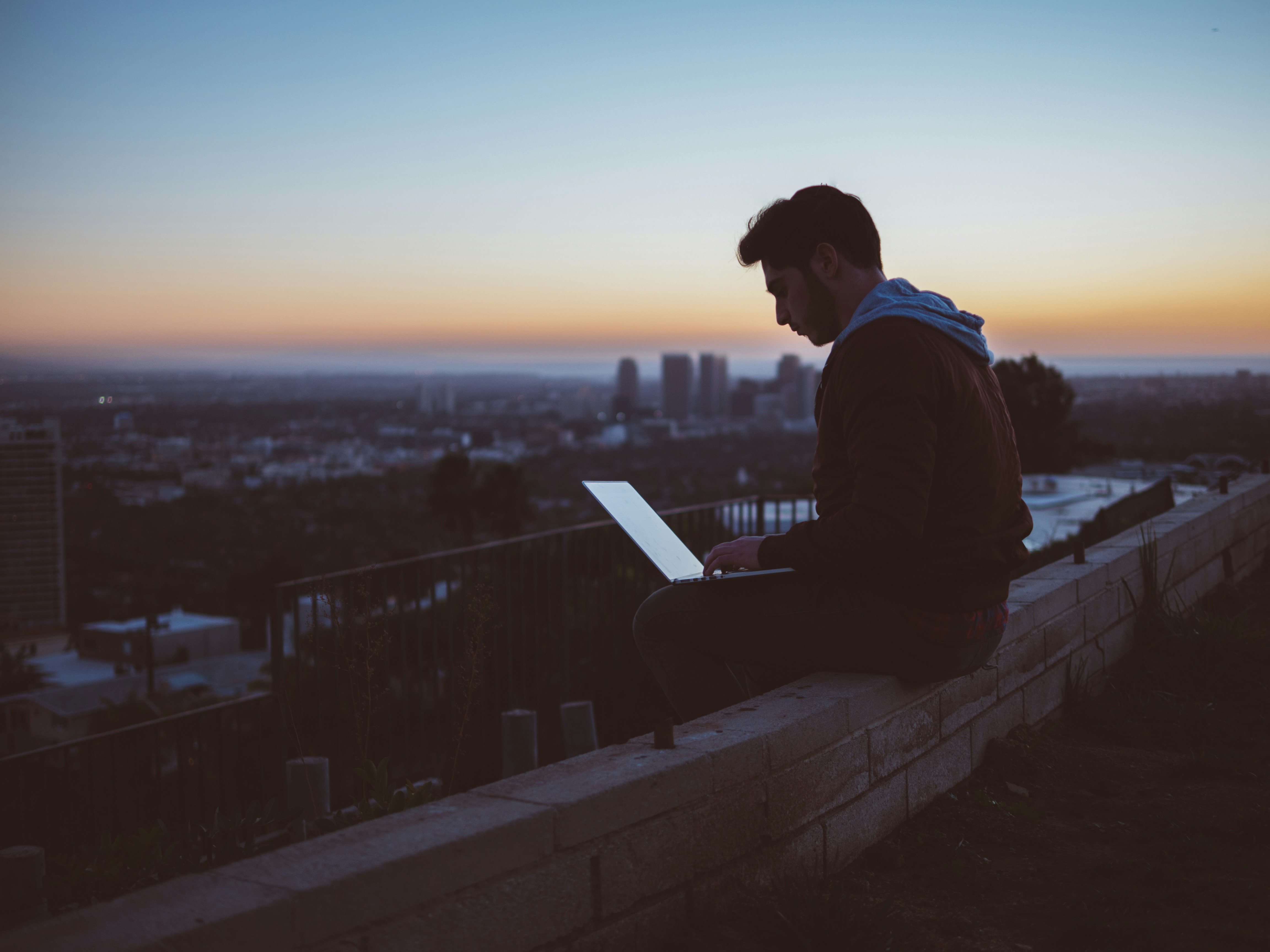 A man working on a computer at dusk outside with a city landscape behind him demonstrating a healthy work-life balance.